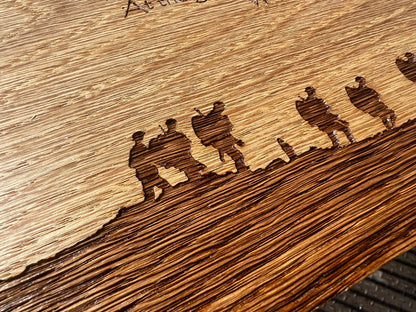 Close-up of engraved soldier silhouettes along an oak remembrance plaque