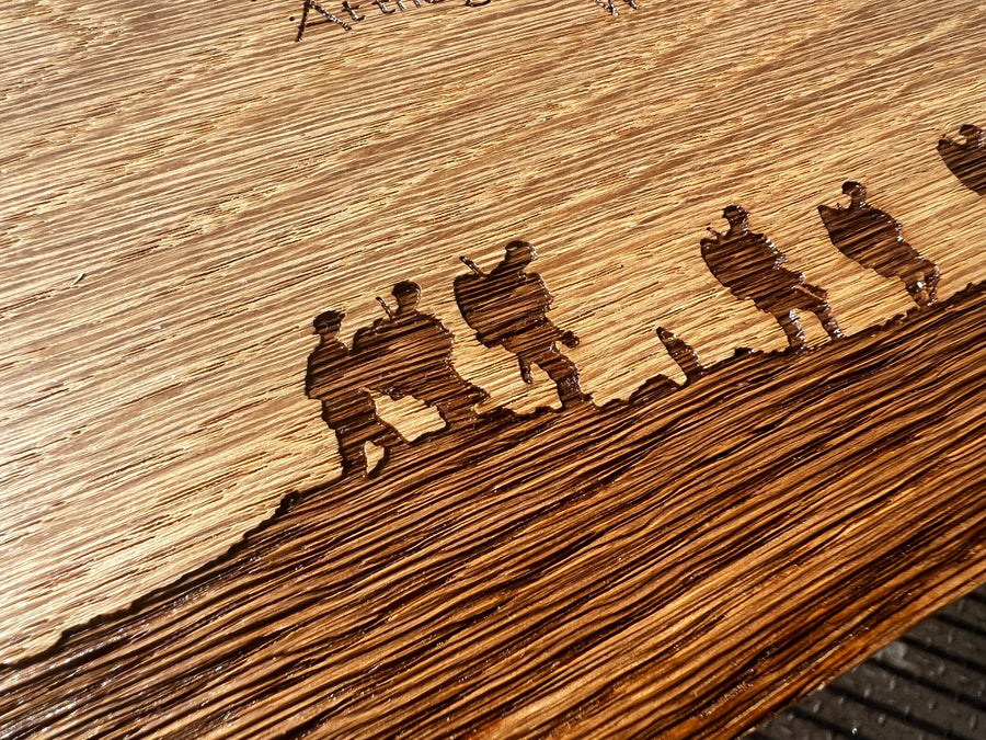 Close-up of engraved soldier silhouettes along an oak remembrance plaque