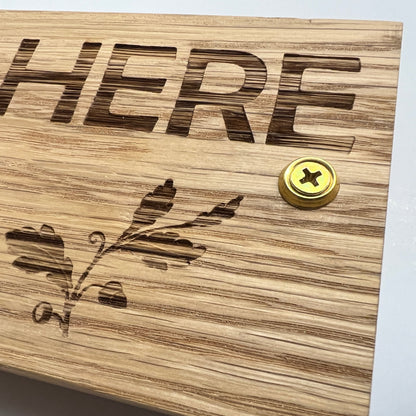 Close-up of engraved lettering, leaf clipart and a fixing screw on oak
