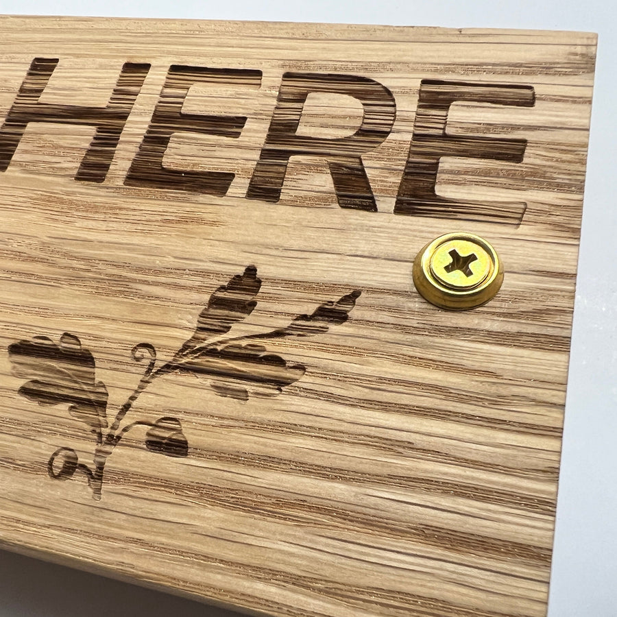 Close-up of engraved lettering, leaf clipart and a fixing screw on oak