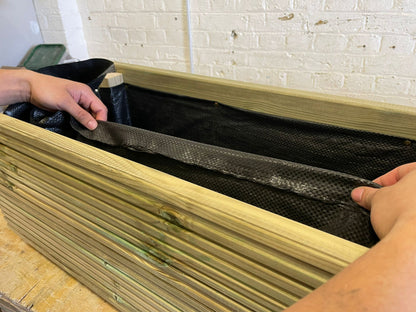 Hands fitting a black liner inside a wooden garden planter